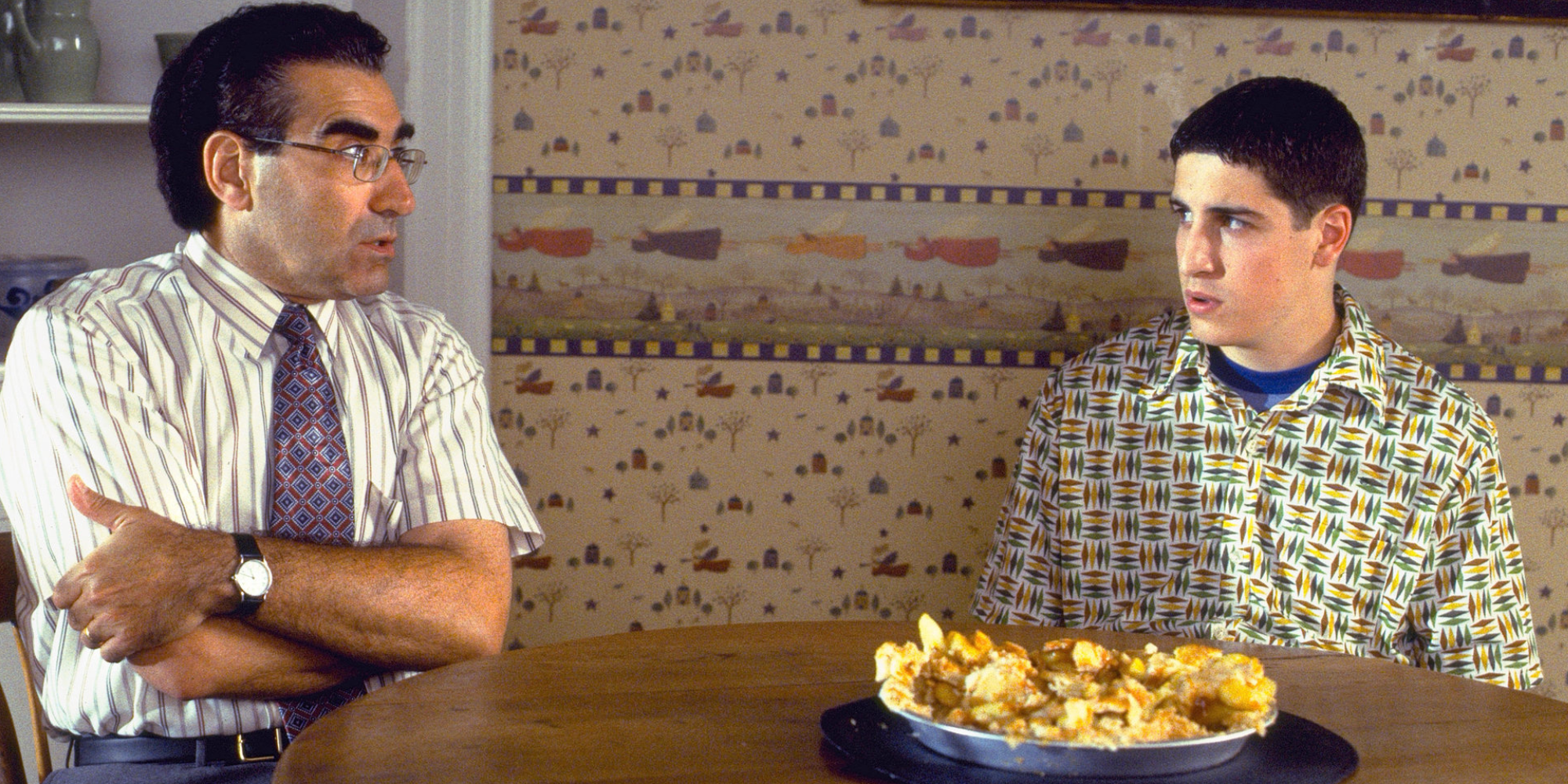 Un tata si fiul sau adolescent poarta o conversatie incomoda in timp ce o placinta cu mere stricata sta pe masa din bucatarie.